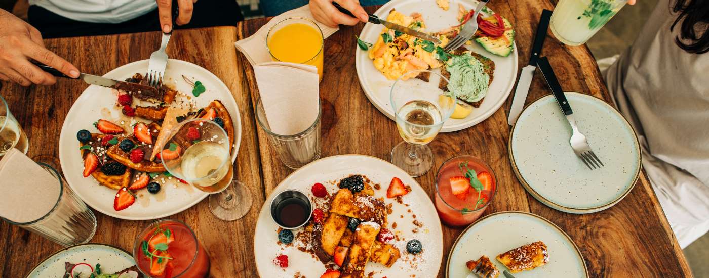 Plates, glasses and people's hands can be seen around a table. 