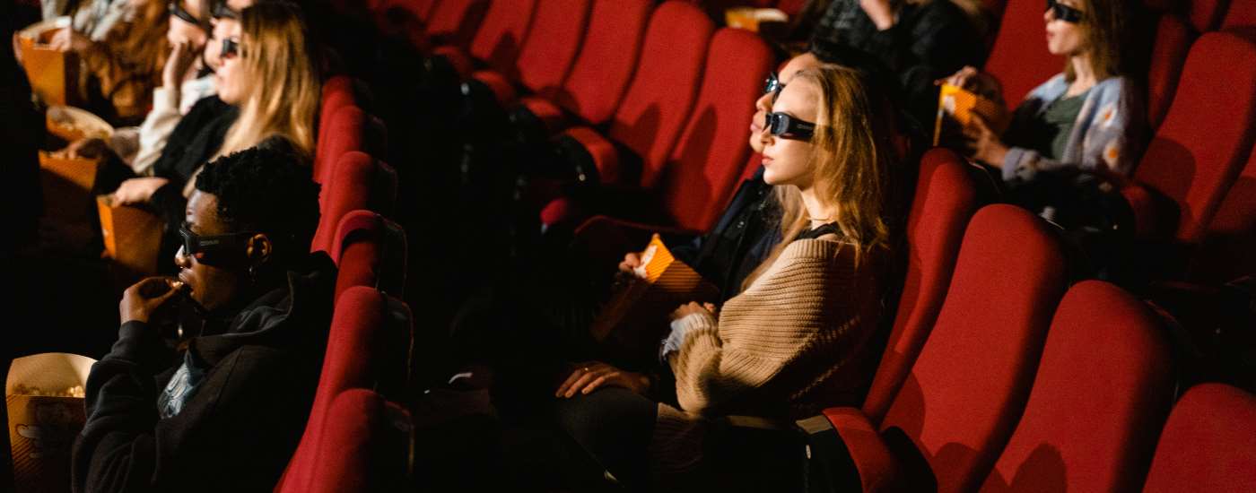 People sit in red cinema chairs looking at a screen.