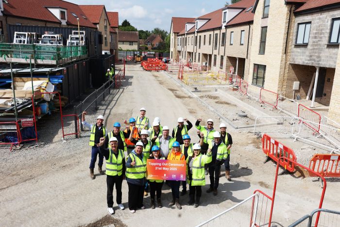 Reps from OCC, OX Place and Lucy Developments celebrate 'topping out' of homes at Marston Paddock. They are standing in PPE on construction site around sign with all logos and cheering towards camera