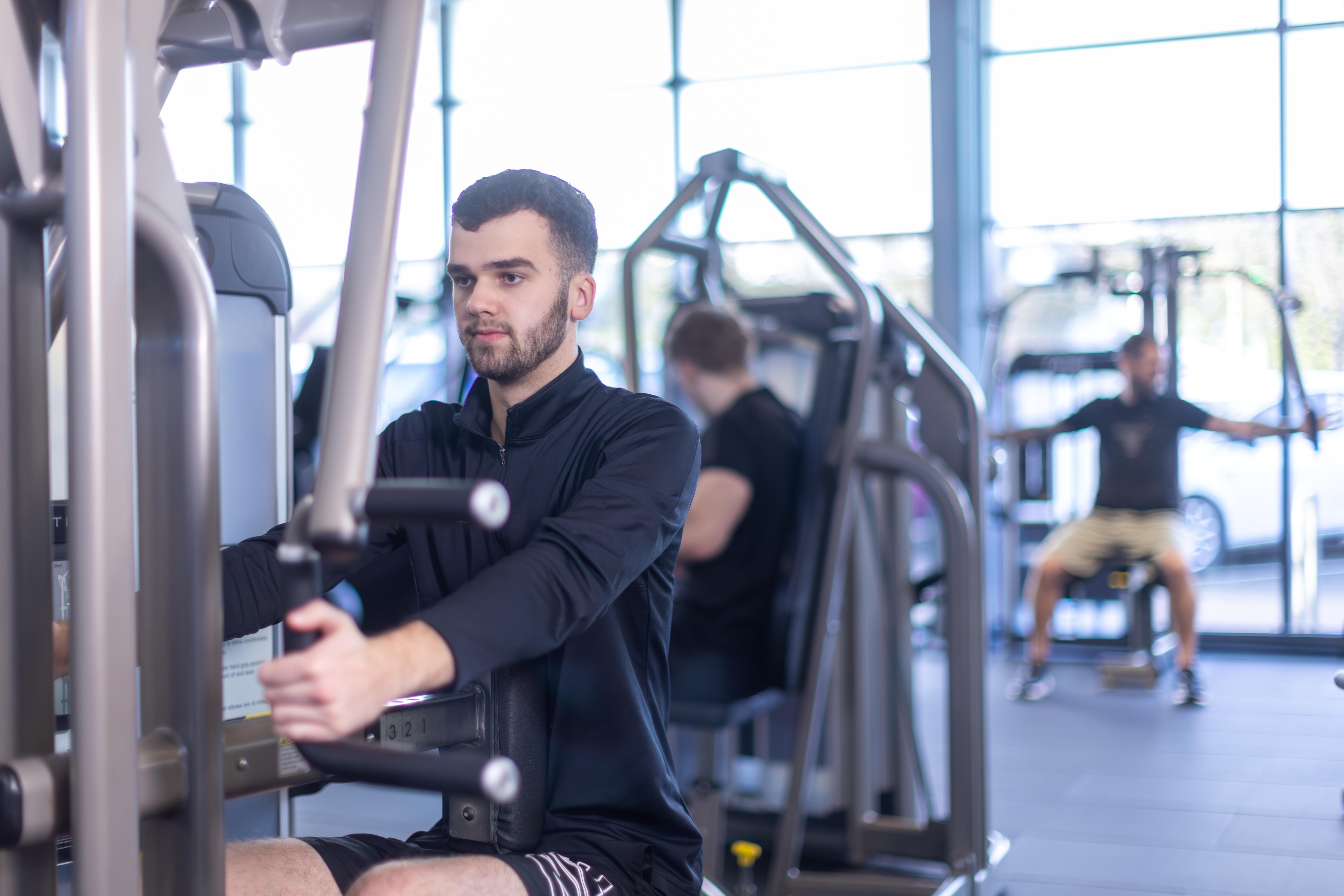 A photo of a white man with dark hair using gym equipment