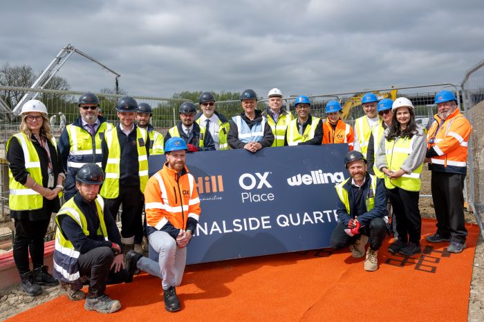 Representatives from OCC, OX Place and The Hill Group in hi-viz and hard hats gather around a sign with logos celebrating milestone